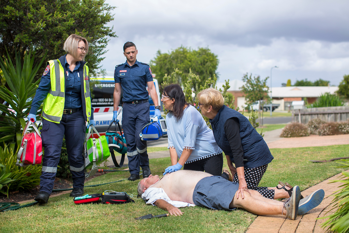 Two paramedics arrive while two women give CPR to a man on the ground.