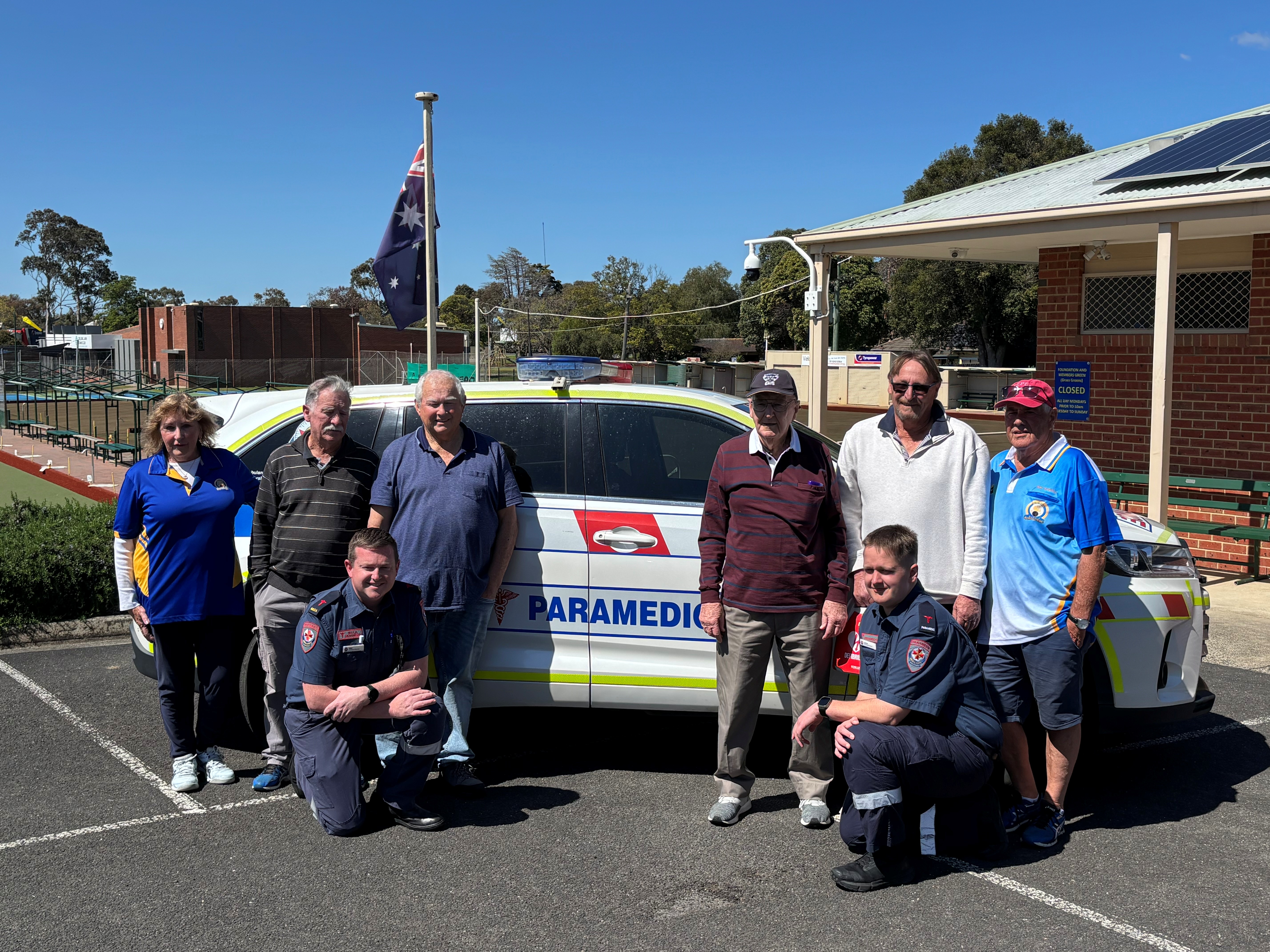 A group of eight people in front of an ambulance car.
