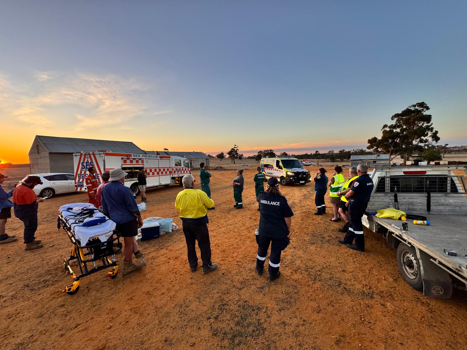 A group of first responders look on at an ambulance and helicopter in the distance.